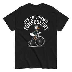 Peut inclure: T-shirt noir avec un canard de dessin animé sur un grand-bi. Le canard porte un chapeau haut de forme, une veste et un nœud papillon. Le texte "OFF TO COMMIT TOMFOOLERY" est arqué au-dessus du canard.