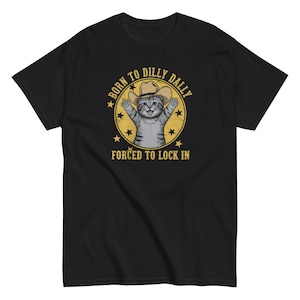 May include: Black t-shirt featuring a cartoon cat wearing a cowboy hat, with the text "BORN TO DILLY DALLY" above and "FORCED TO LOCK IN" below. The design is in a yellow circle with stars.