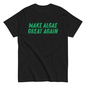 May include: A black short-sleeved t-shirt featuring the text "MAKE ALGAE GREAT AGAIN" printed in a distressed, textured green font across the centre of the chest. The garment has a crew neckline and a standard fit with short sleeves.