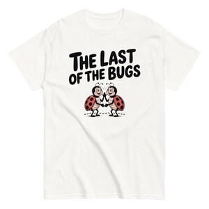 Peut inclure: Un t-shirt blanc avec le texte noir THE LAST OF THE BUGS au-dessus d'un dessin de deux coccinelles de dessin animé aux ailes rouges à pois noirs, debout sur leurs pattes arrière et se faisant un check avec leurs pattes avant.