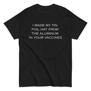 May include: Black t-shirt with white text that reads: "I MADE MY TIN FOIL HAT FROM THE ALUMINUM IN YOUR VACCINES". The shirt is a short-sleeved crew neck.