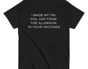 May include: Black t-shirt with white text that reads: "I MADE MY TIN FOIL HAT FROM THE ALUMINUM IN YOUR VACCINES". The shirt is a short-sleeved crew neck.