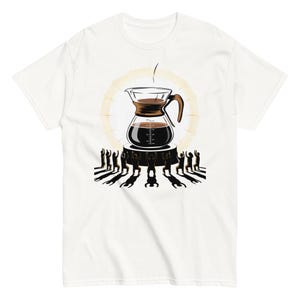 Peut inclure: T-shirt blanc avec une illustration sur le thème du café. Une carafe en verre contenant du café brun est posée sur un piédestal, entourée de silhouettes. Un halo doré entoure la carafe, avec un filet de café qui s'y verse.