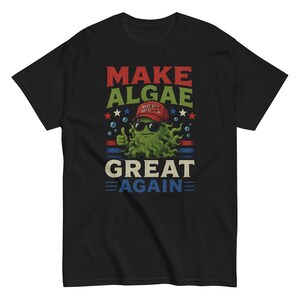 Peut inclure: Un t-shirt noir à manches courtes avec un motif représentant une algue verte portant une casquette rouge et des lunettes de soleil, faisant un pouce levé. Le texte indique MAKE ALGAE GREAT AGAIN, avec des étoiles et des rayures bleu-blanc-rouge.