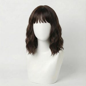 May include: A shoulder-length dark brown wig with soft, loose waves and straight-cut bangs. The hair is styled with a centre part and rests on a smooth, white, featureless mannequin head, showcasing a natural-looking texture and volume.