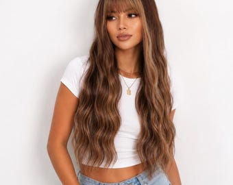May include: A long, wavy brown wig with lighter blonde highlights and straight-cut bangs. The hair features a multi-tonal color blend with darker roots transitioning into lighter brown and blonde lengths, styled in loose, flowing waves.