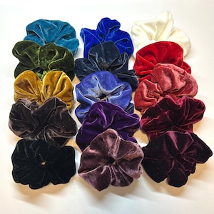 May include: A collection of fifteen velvet hair scrunchies arranged in three columns. The colors include teal, olive green, mustard yellow, dark brown, black, royal blue, navy, periwinkle, purple, mauve, white, bright red, rose, burgundy, and maroon.