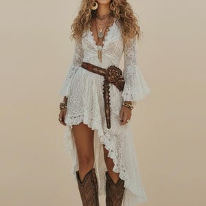 Könnte beinhalten: Ein weißes Spitzenkleid mit langen Ärmeln und einem High-Low-Saum. Das Kleid wird mit einem braunen Gürtel, Cowboystiefeln und einem breitkrempigen Hut kombiniert. Die Person trägt mehrere Halsketten und Armbänder.