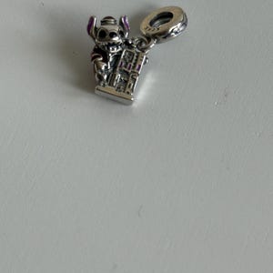 Puede incluir: Un charm de plata con el personaje Stitch de la pel&iacute;cula Lilo & Stitch. El charm muestra a Stitch sosteniendo un edificio, con detalles morados en sus orejas y ropa. El charm tiene un lazo para sujetarlo a una pulsera o collar.