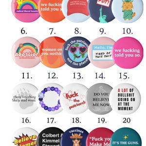 Puede incluir: Una colección de veinte botones redondos con varios diseños y texto. Los botones presentan un arcoíris, un gato de la Estatua de la Libertad y frases como "We fuckin told you so". Los colores incluyen rosa, naranja, azul y verde.