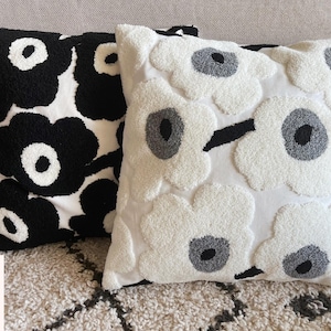 May include: Two decorative throw pillows with a floral pattern. One pillow is black and white with large, bold flowers. The other pillow is white with gray and white flowers.