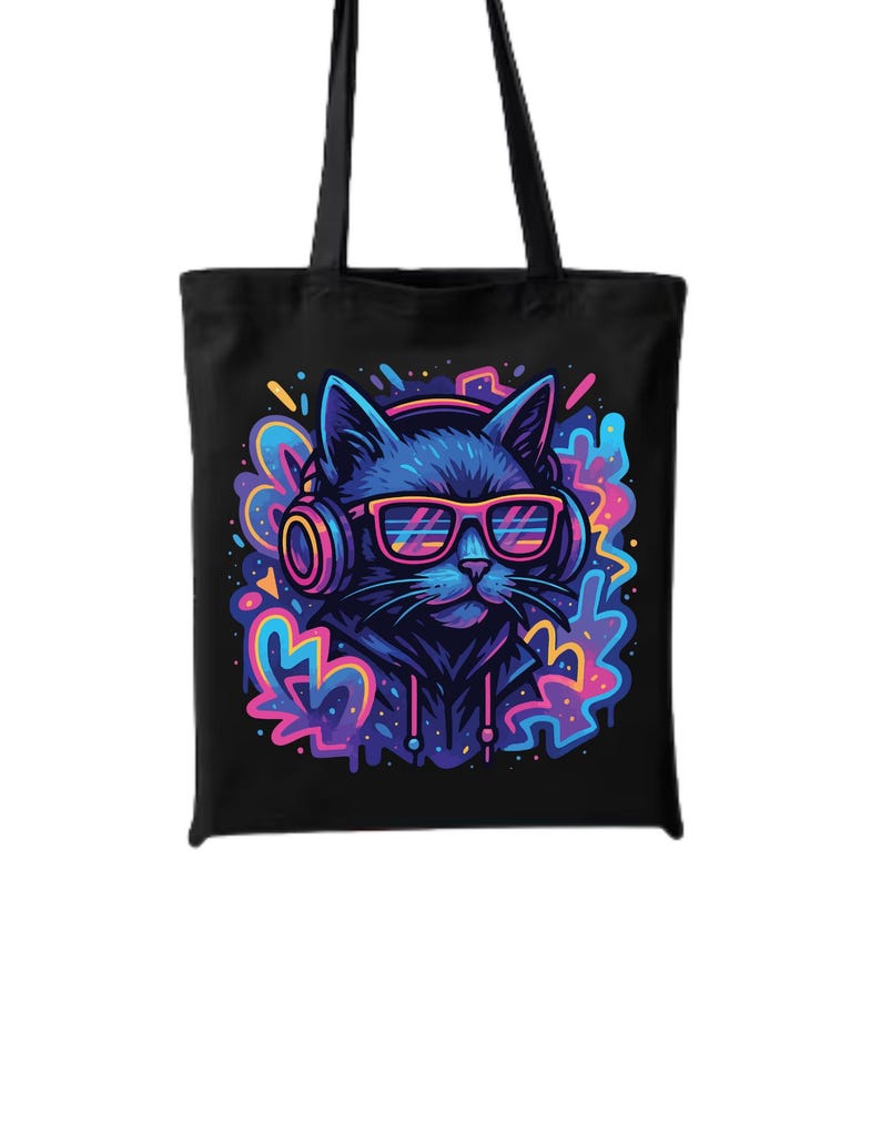 May include: Black tote bag featuring a vibrant illustration of a cat wearing headphones and sunglasses. The cat is surrounded by colorful, abstract shapes in shades of blue, pink, and purple. The bag has two black handles.