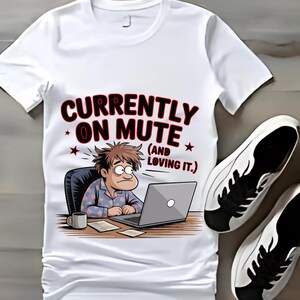 Könnte beinhalten: Weißes T-Shirt mit einer Cartoon-Grafik einer Person, die an einem Laptop arbeitet, mit dem Text "CURRENTLY ON MUTE (AND LOVING IT.)". Das Bild zeigt auch ein Paar weißer und schwarzer Turnschuhe.