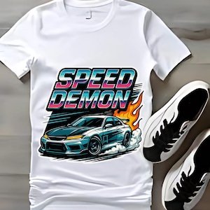 Könnte beinhalten: Weißes T-Shirt mit einer Grafik eines blauen Sportwagens, Flammen und dem Text "SPEED DEMON". Ein Paar weiße Turnschuhe mit schwarzen Akzenten liegen neben dem Shirt.