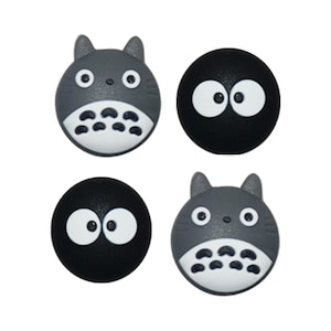 May include: Four decorative buttons featuring characters from a popular animated film. Two buttons are grey with cat-like faces and white bellies. The other two are black with large white eyes. All buttons have a rounded shape.