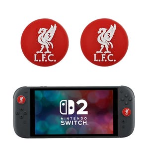 May include: A grey Nintendo Switch console with two red thumb grips, each displaying a white bird emblem and the letters "L.F.C." The console has the Nintendo Switch logo and the number "2" in white. The bird logo is also on the console.