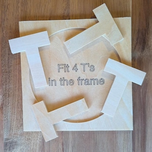 May include: A wooden puzzle with the text "Fit 4 T's in the frame". The puzzle consists of a square wooden base with a circular cutout and four wooden "T" shaped pieces scattered around the base.