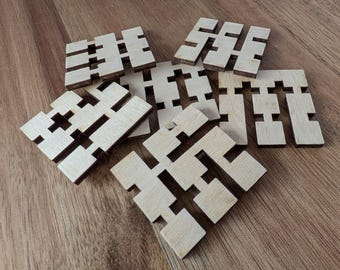 May include: A collection of interlocking wooden puzzle pieces. The pieces are light-colored with a darker edge, arranged on a wooden surface. The shapes are geometric and designed to fit together, suggesting a brain teaser or educational toy.
