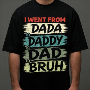 May include: Black t-shirt with the text "I went from Dada to Daddy to Dad to Bruh" in a distressed, brushstroke style. The text is in red, cream, teal, and green. A casual, humorous apparel item.