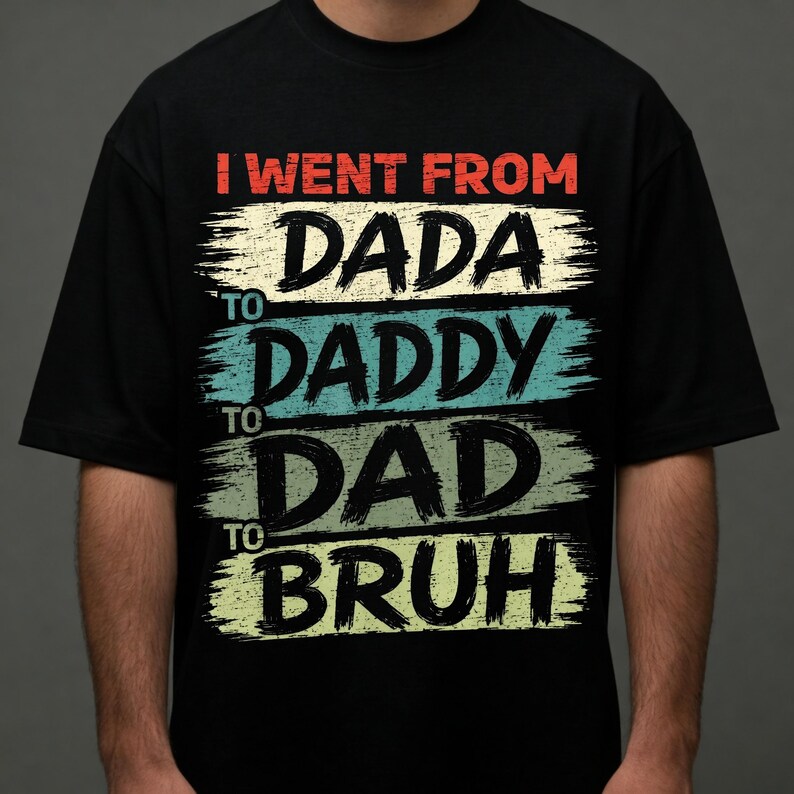 May include: Black t-shirt with the text "I went from Dada to Daddy to Dad to Bruh" in a distressed, brushstroke style. The text is in red, cream, teal, and green. A casual, humorous apparel item.