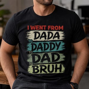 May include: Black t-shirt with the text "I WENT FROM DADA TO DADDY TO DAD TO BRUH" in red, white, teal, and yellow-green. The text is layered on top of each other with a brush stroke effect.