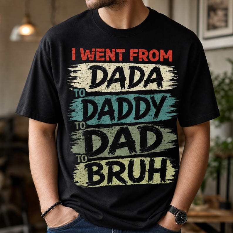 May include: Black t-shirt with the text "I went from Dada to Daddy to Dad to Bruh" in a distressed, multi-colored design. The text is layered on horizontal stripes of red, cream, teal, and green.