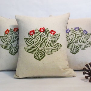 Puede incluir: Tres almohadas decorativas con fondo blanco y diseño floral verde. Las almohadas presentan un loto estilizado con flores rojas, moradas y azules.