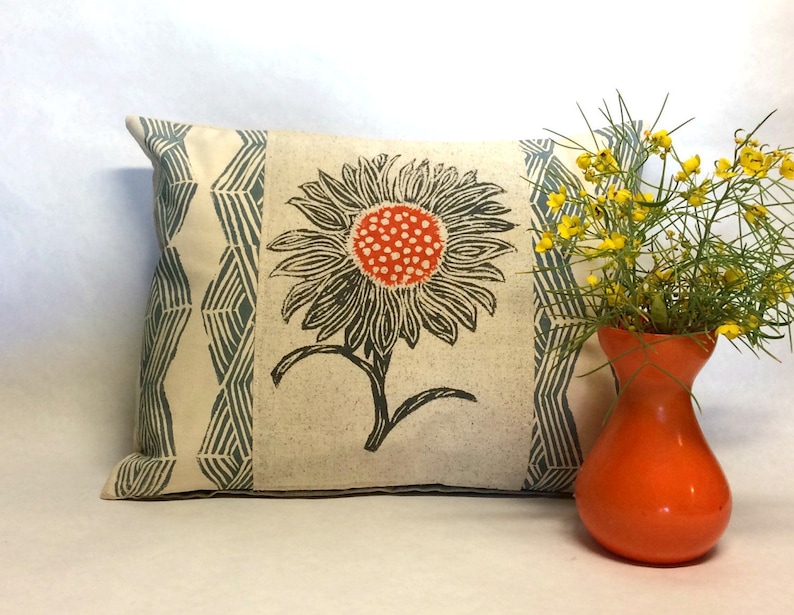 May include: A decorative pillow with a white background and a blue and white geometric pattern. The pillow features a large, orange and black floral print of a sunflower.