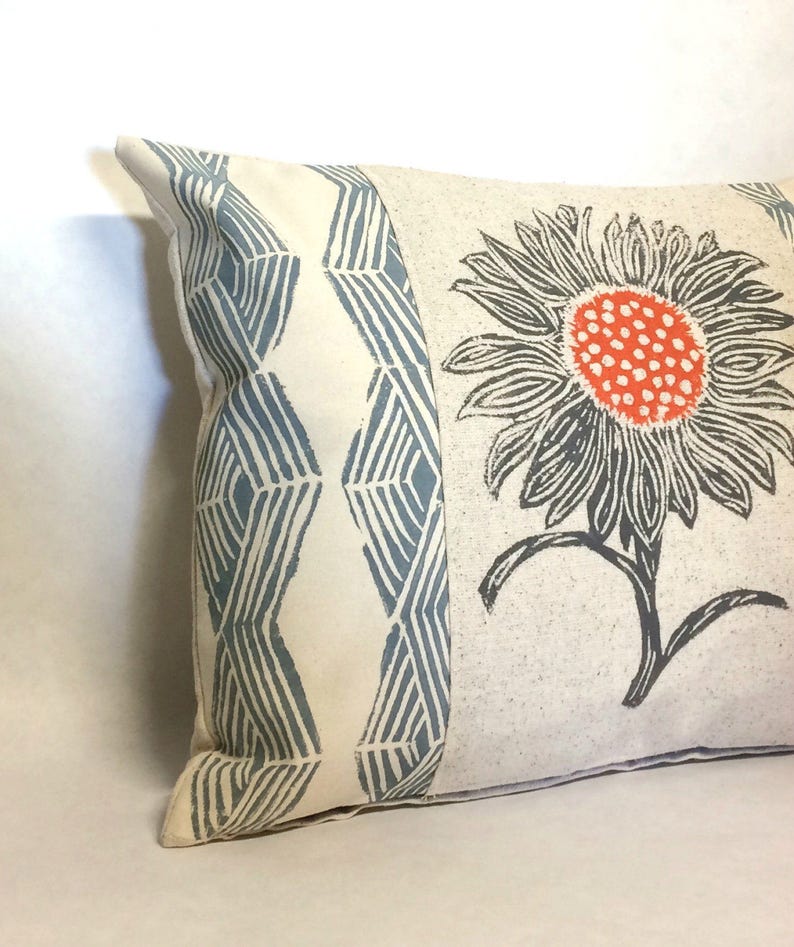 May include: A white pillow with a blue and white geometric pattern on one side and a large orange and gray flower on the other side.