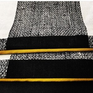 May include: Close up of black and white checkered fabric with a yellow trim. The fabric has a textured, woven look.