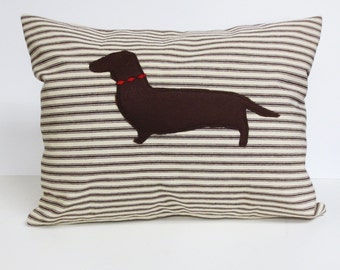 May include: A brown and white striped pillow with a brown dachshund silhouette appliqué. The dachshund has a red collar.