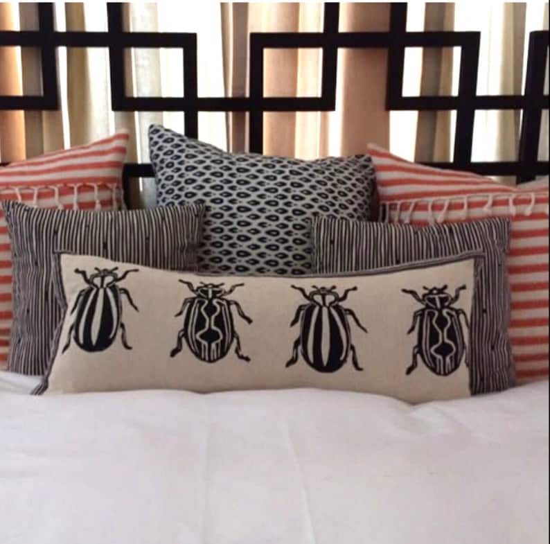 Puede incluir: Una cama blanca con una cabecera de metal negro y una variedad de almohadas. Las almohadas son a rayas, estampadas y presentan un dise&ntilde;o de escarabajo blanco y negro.