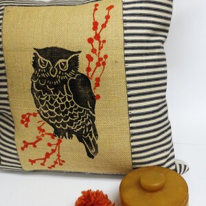 May include: A decorative pillow with a black and white owl design on a burlap background. The owl is perched on a branch with red berries. The pillow has a black and white striped border.