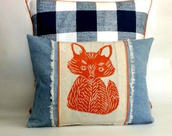 May include: Two decorative throw pillows. The top pillow is white and black buffalo plaid. The bottom pillow is blue denim with a white and orange fox print.
