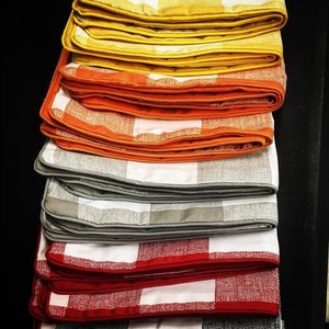 May include: A stack of eight checkered fabric cushions in various colors, including yellow, orange, gray, and red. The cushions are folded and stacked on top of each other, with the yellow cushions at the top and the red cushions at the bottom. The cushions have a checkered pattern and are trimmed with a contrasting color.