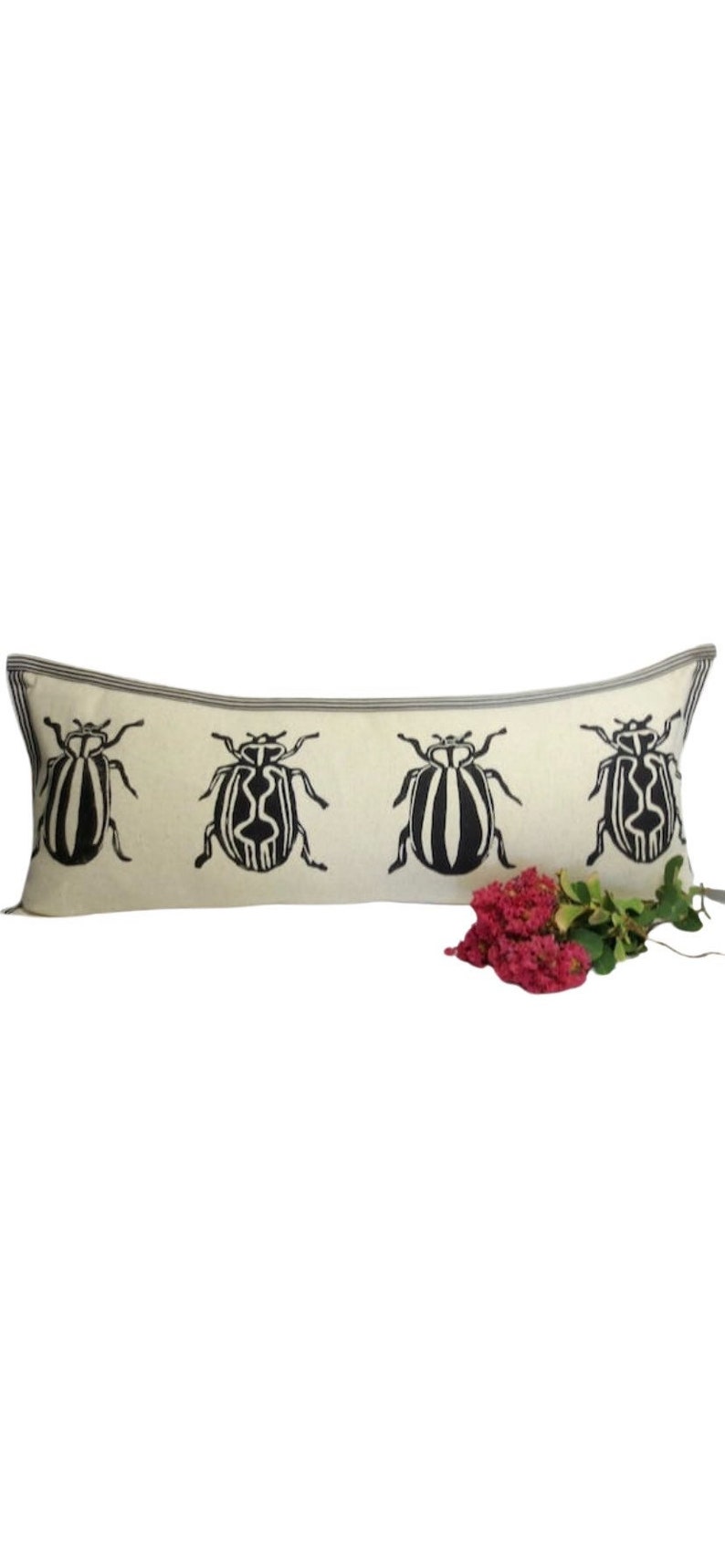 Puede incluir: Una almohada larga y rectangular con fondo blanco y dise&ntilde;os de escarabajos negros. La almohada tiene una franja gris a lo largo de los bordes.
