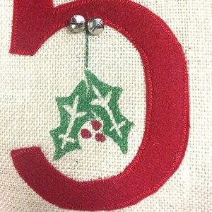 May include: A red felt number five with a green holly leaf design and two silver jingle bells hanging from the top.