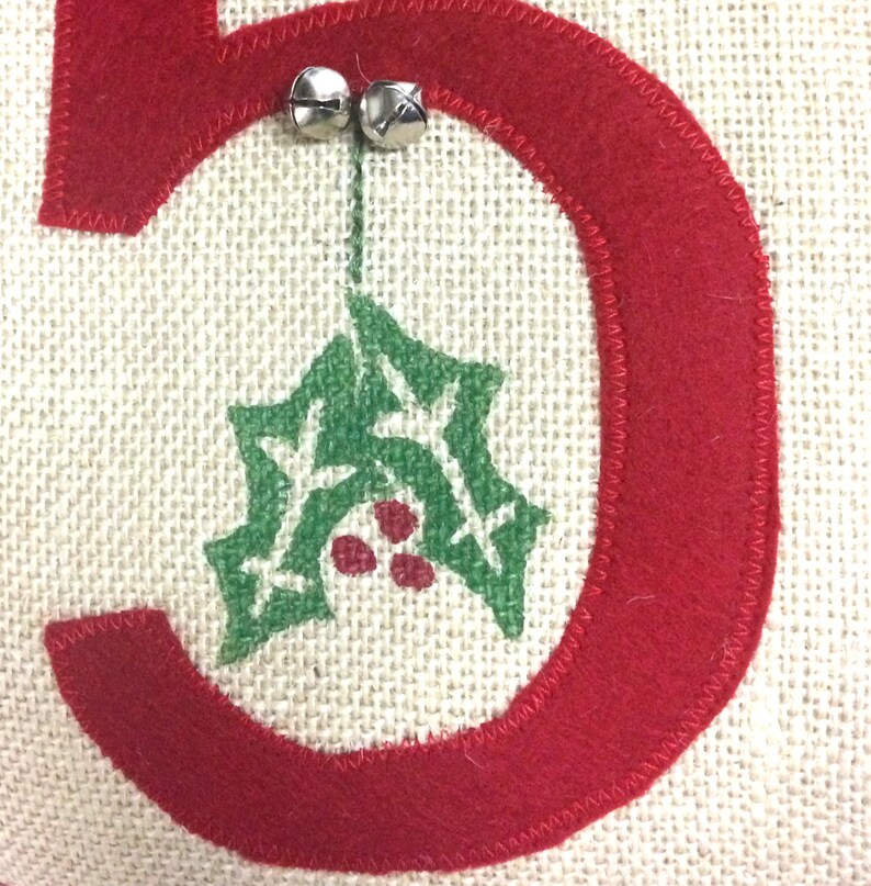 May include: A red felt number five with a green holly leaf design and two silver jingle bells hanging from the top.