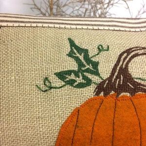 Op de afbeelding: Een jute kussen met een oranje viltpompoen en groene viltbladeren. De pompoen heeft een bruine viltstengel.