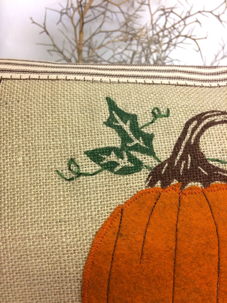 Op de afbeelding: Een jute kussen met een oranje viltpompoen en groene viltbladeren. De pompoen heeft een bruine viltstengel.