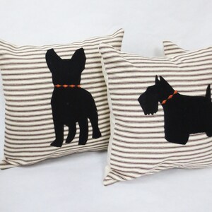 May include: Two decorative throw pillows with black silhouette images of dogs. The pillows have a white background with brown stripes. One pillow features a French Bulldog and the other a Scottish Terrier.