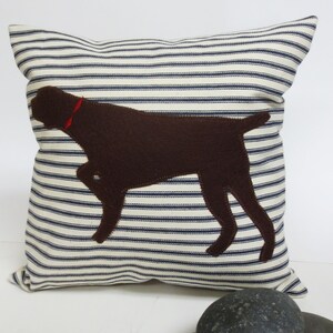 May include: A white and blue striped cushion with a brown felt silhouette of a dog on it.
