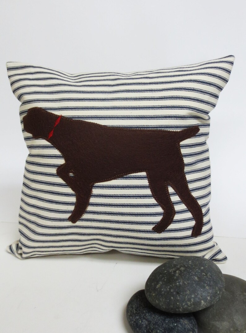 May include: A white and blue striped cushion with a brown felt silhouette of a dog on it.