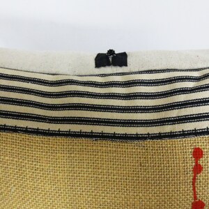 May include: A close-up of a pillow with a black and white striped fabric and a burlap fabric with red dots. The pillow has a black fabric loop at the top.