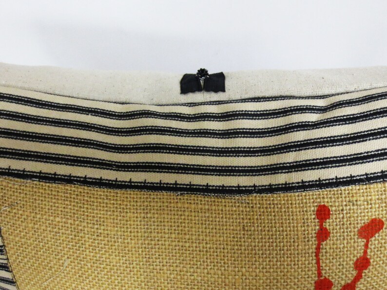 May include: A close-up of a pillow with a black and white striped fabric and a burlap fabric with red dots. The pillow has a black fabric loop at the top.