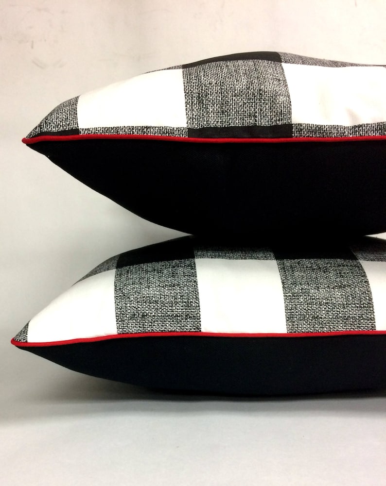 May include: Two black and white checkered throw pillows with red piping. The pillows are stacked on top of each other with the top pillow slightly offset to the right. The pillows have a black backing.