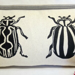 Puede incluir: Una almohada lumbar blanca con un dise&ntilde;o de escarabajo rayado en blanco y negro que se repite en la tela. La almohada est&aacute; hecha de una tela suave y natural.