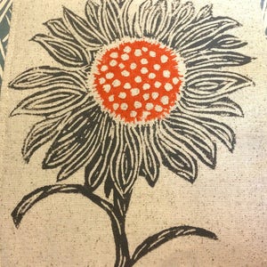 May include: A black and white printed sunflower with an orange center on a beige fabric background.