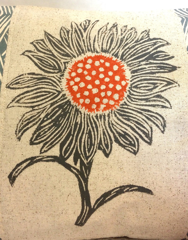 May include: A black and white printed sunflower with an orange center on a beige fabric background.