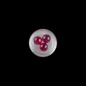 Puede incluir: Tres piedras preciosas redondas de color rojo en un recipiente de plástico transparente.